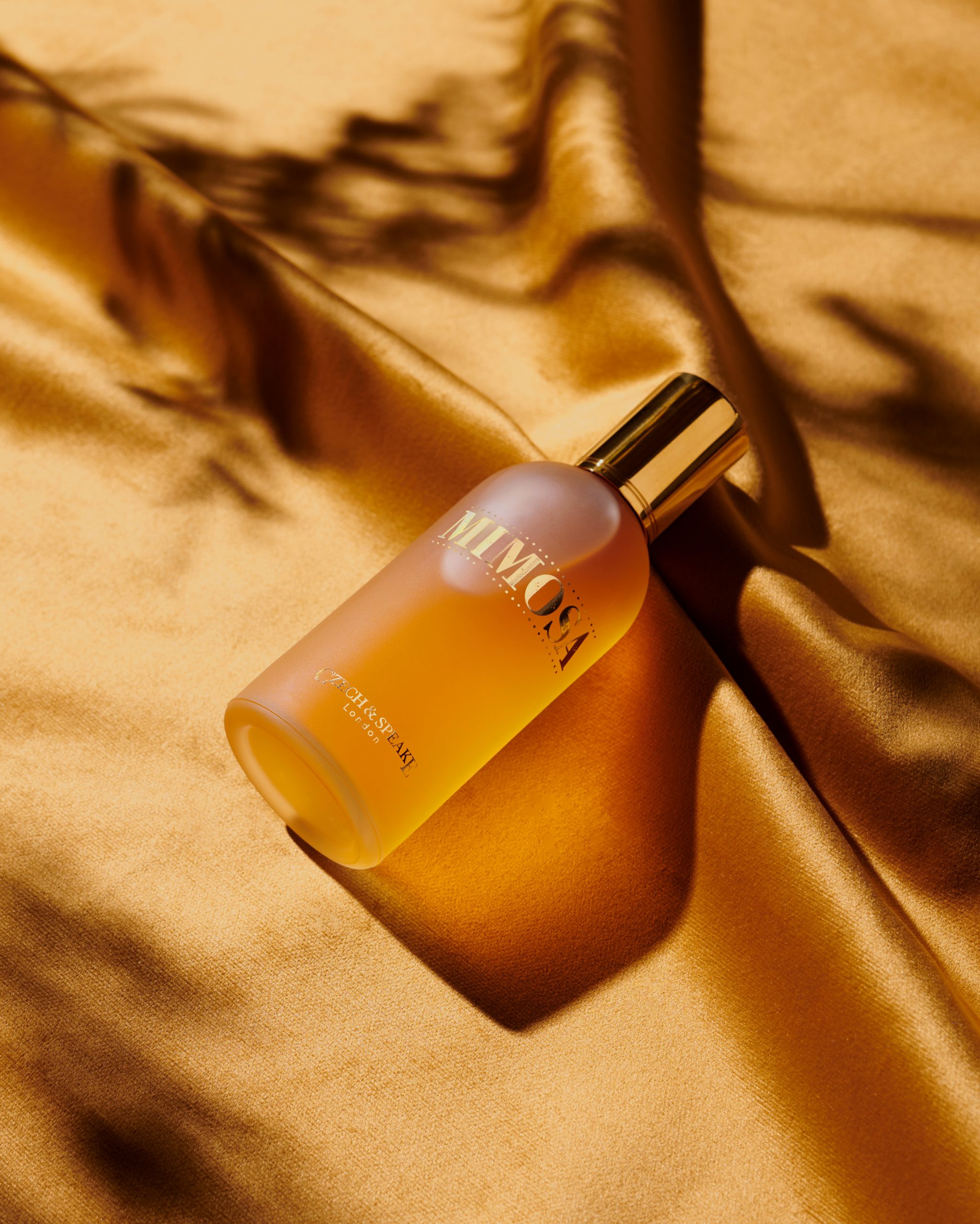 Mimosa perfume bottle lying on gold velvet under tree