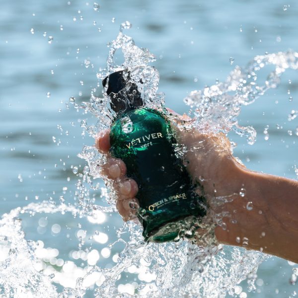 Green vetiver fragrance bottle in hand in ocean