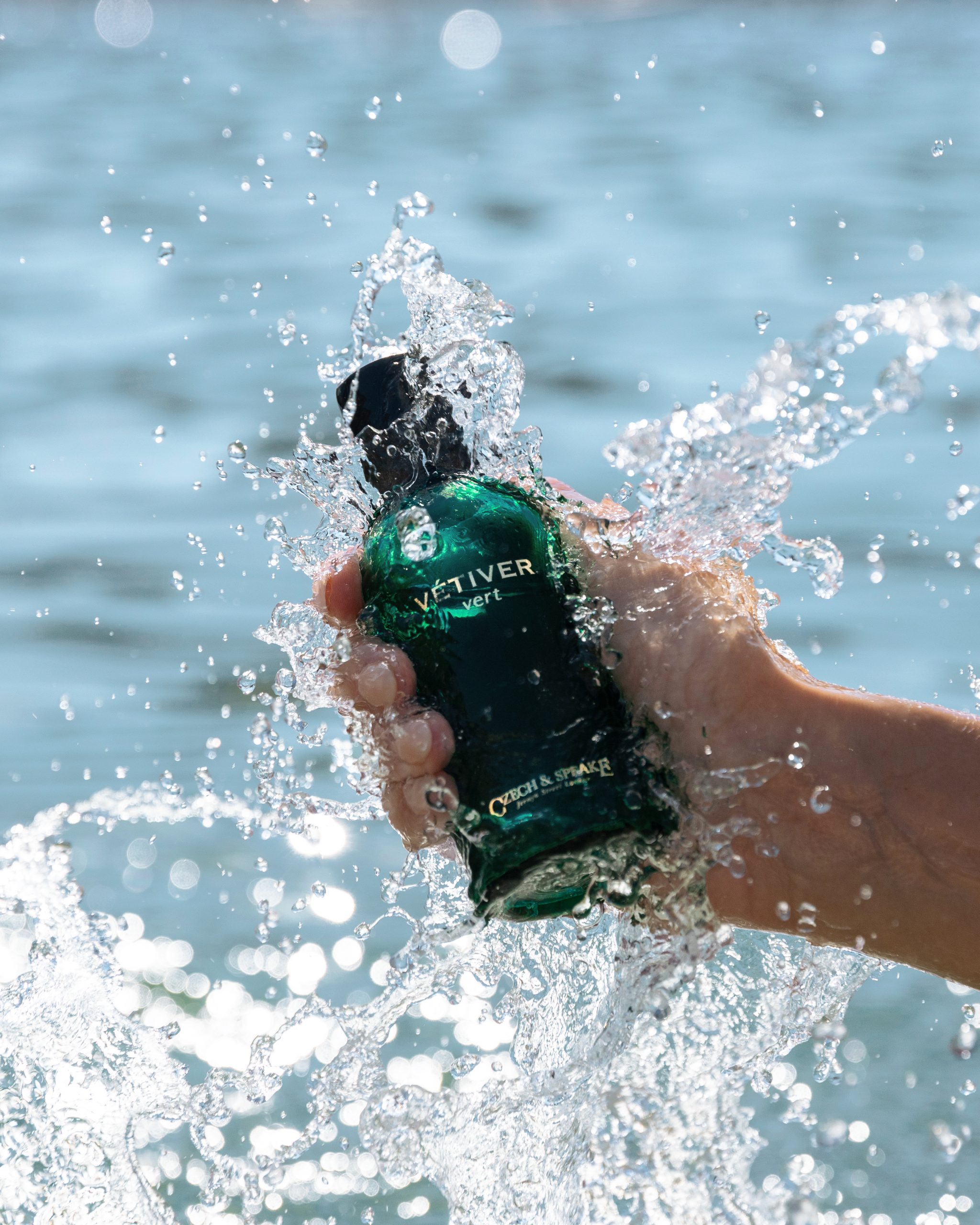 Green vetiver fragrance bottle in hand in ocean