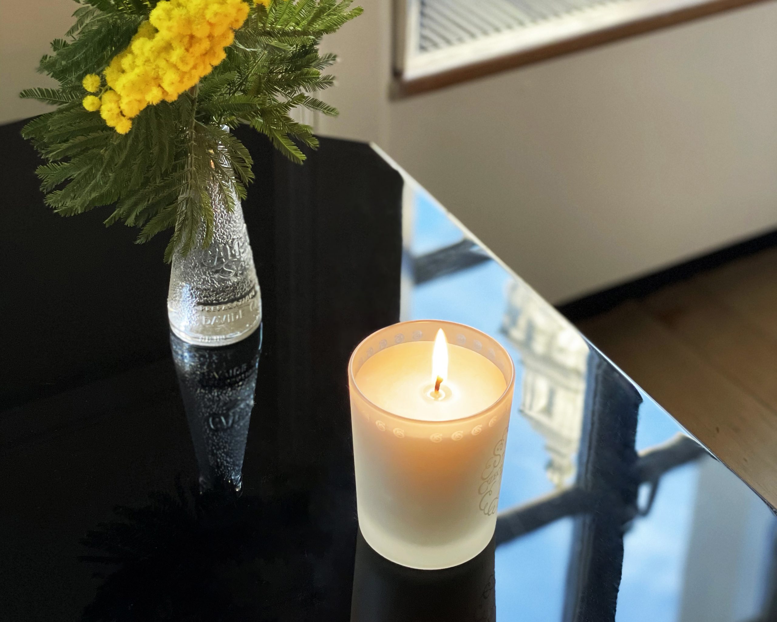 Czech & Speake fragrant candle on black table with vase of yellow flowers